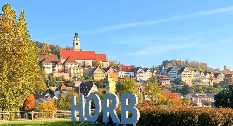 Eine hügelige Stadtlandschaft mit traditionellen Häusern, einem Kirchturm und dem Schriftzug "HORB" im Vordergrund.