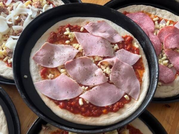 Mehrere Pizzen mit rotem Tomatensugo, Käse und verschiedenen Belägen wie Schinken, Salami und Thunfisch auf Holzuntergrund.