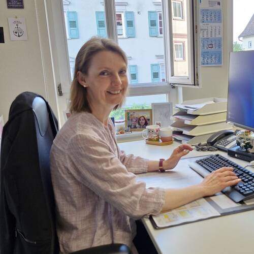 Portrait von einer Frau am Schreibtisch in einem hellen modernen Büroraum vor einem Bildschirm und Tastatur