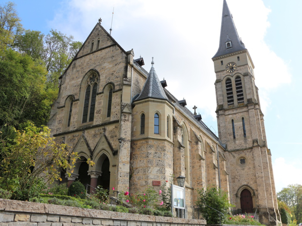Das Bild zeigt eine Kirche umgeben von Bäumen und Sträuchern.