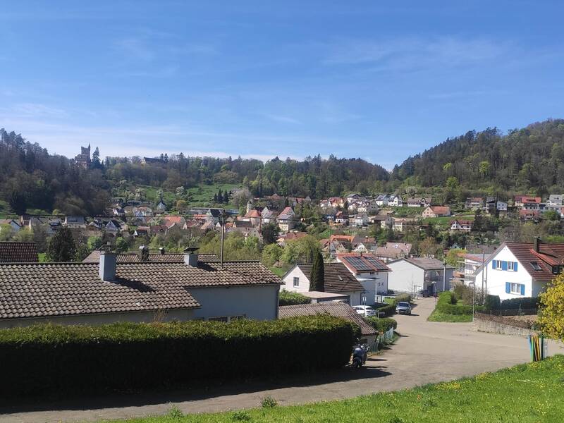 Landschaft mit Häusern bei blauem Himmel. Im Hintergrund ist ein Schloss zu sehen.