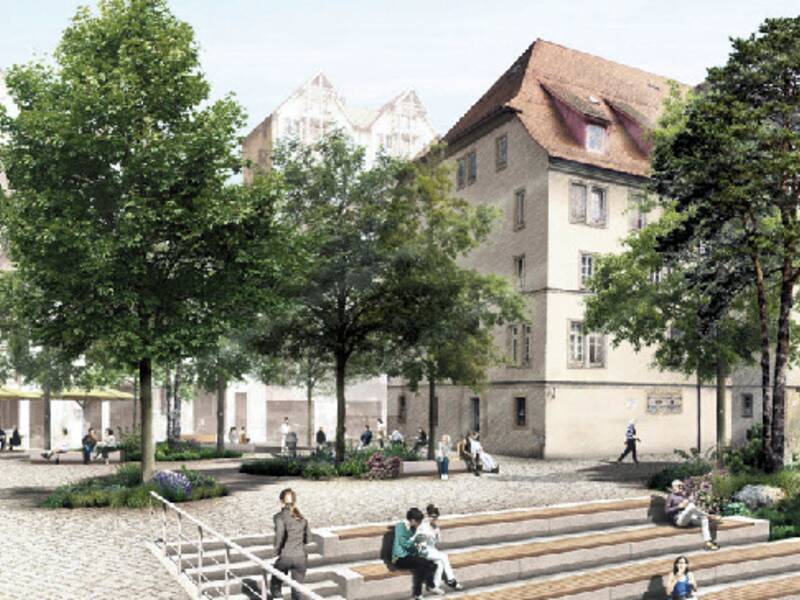 Stadtplatz mit Stufen, Bäumen und historischen Fachwerkhäusern im Hintergrund, Menschen sitzen und gehen spazieren.