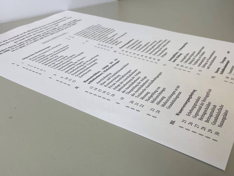 Ein Blatt Papier mit einem mehrspaltigen Text und Listen, liegend auf einem grauen Tisch.