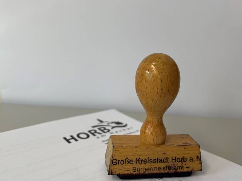 Holzstempel mit der Aufschrift 'Große Kreisstadt Horb a. N. - Bürgermeisteramt' auf einem weißen Papier mit dem Schriftzug 'HORB'.