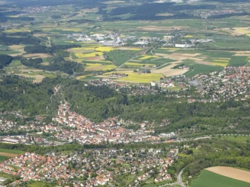 Luftaufnahme einer Stadt mit mehreren Stadtteilen, umgeben von Feldern und Wäldern.