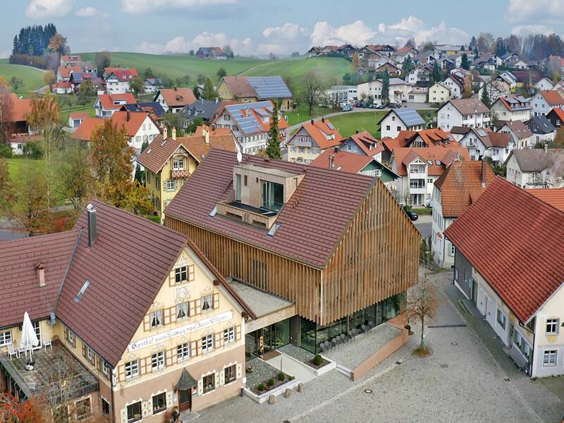 Dorf mit traditionellen und modernen Häusern, umgeben von grünen Feldern und Hügeln unter bewölktem Himmel.