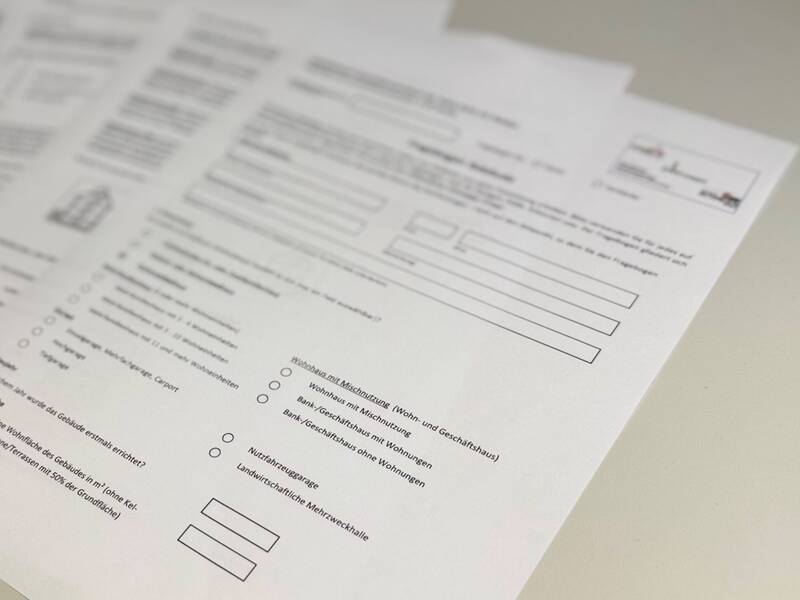 Auf dem Bild sind mehrere gestapelte Formularblätter mit Text und Auswahlkästchen zu sehen, die auf einem Tisch liegen.