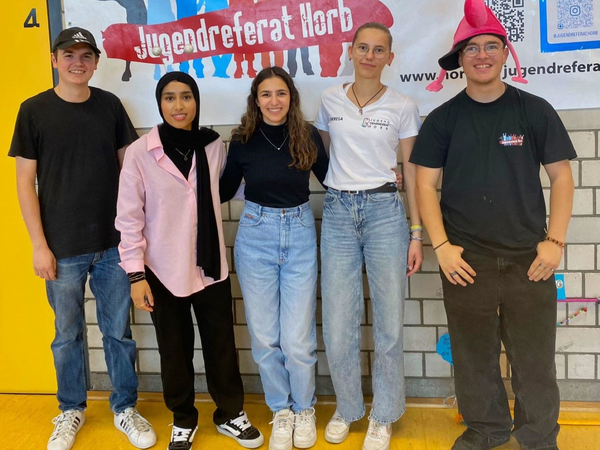 Fünf junge Menschen stehen lächelnd vor einem Plakat des Jugendreferats Horb.