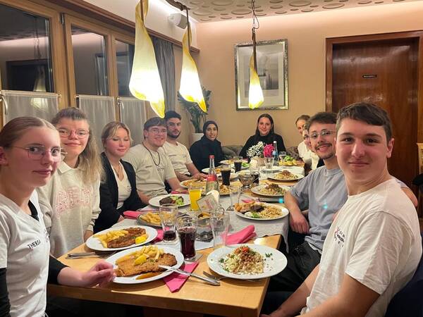 Eine Gruppe von jungen Erwachsenen sitzt fröhlich an einem langen Tisch in einem Restaurant und genießt gemeinsam eine Mahlzeit.