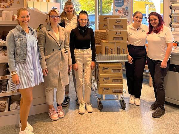 Eine Gruppe von sechs lächelnden Personen steht in einem Geschäft neben einem Einkaufswagen voller Kartons mit der Aufschrift "Jessa".