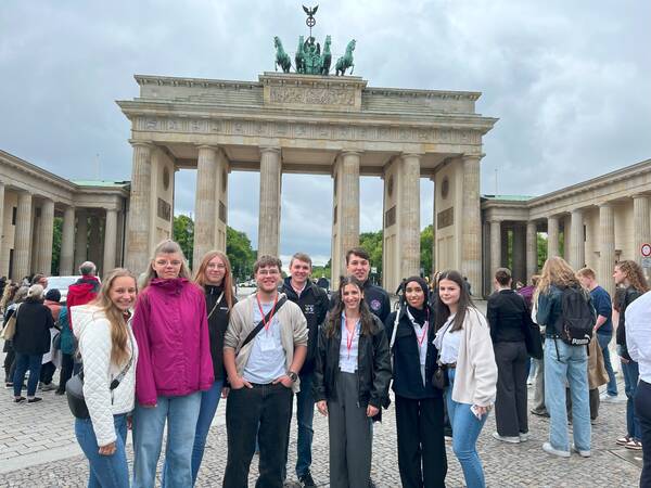 Eine Gruppe von Menschen steht vor dem Brandenburger Tor in Berlin bei bewölktem Himmel.