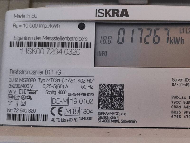 Ein digitaler Stromzähler der Marke ISKRA zeigt einen Verbrauchswert von 17267 kWh an, umgeben von technischen Details und QR-Codes.