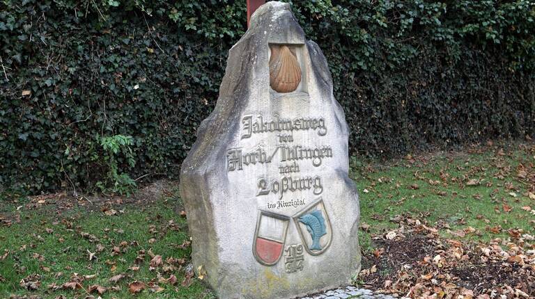 Ein großer, gravierter Gedenkstein am Wegesrand mit der Aufschrift "Jakobsweg von Tübingen nach Rottenburg" und kleinen Wappen darüber und darunter.