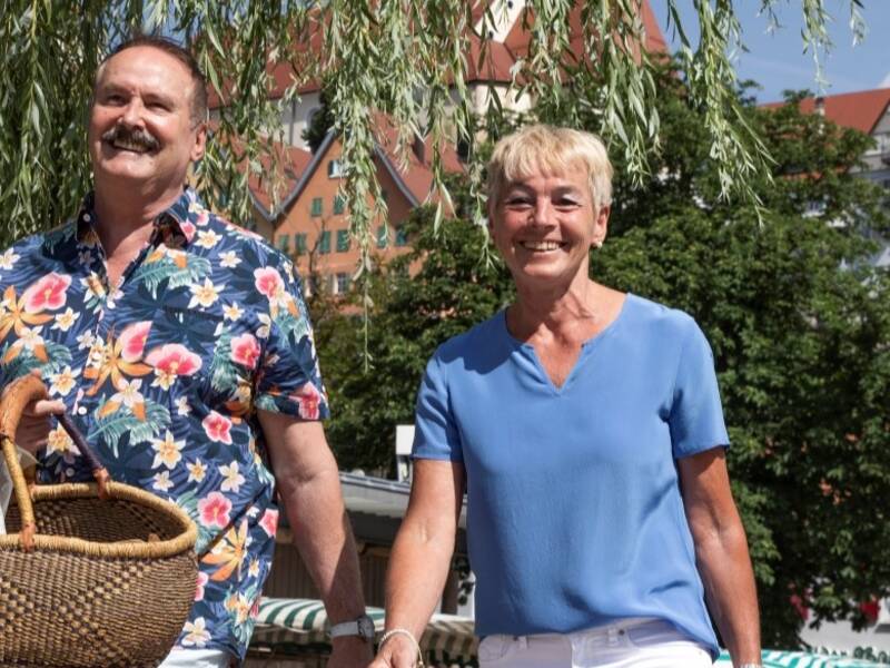 Eine Frau und ein Mann, die lachend in der Stadt laufen und einen Korb in der Hand haben.