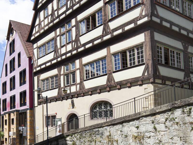 Das Bild zeigt die Horber Altstadtstraße mit einem traditionellen Fachwerkhaus und einem Stadttor im Hintergrund unter blauem Himmel.