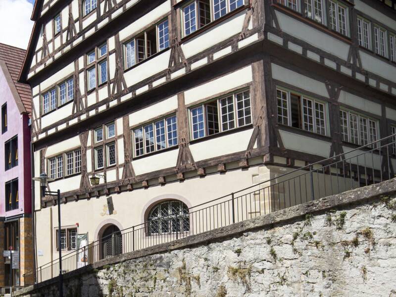 Das Bild zeigt die Horber Altstadtstraße mit einem traditionellen Fachwerkhaus und einem Stadttor im Hintergrund unter blauem Himmel.
