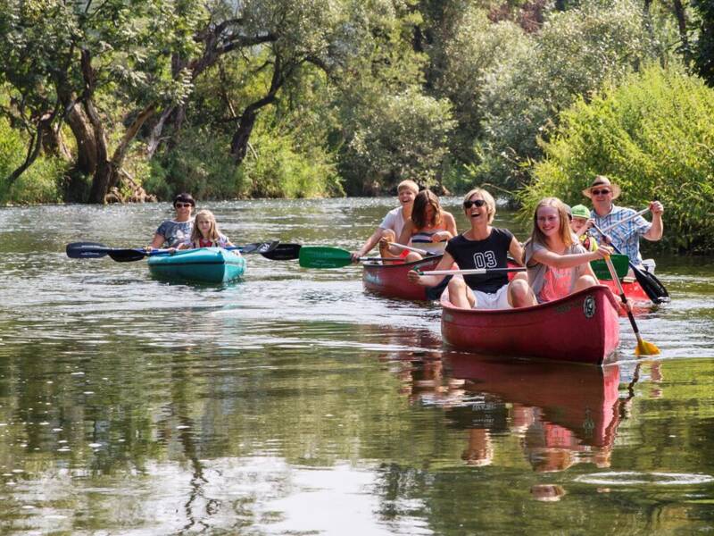 Eine Gruppe von Menschen paddelt in Kanus auf einem von Bäumen gesäumten Fluss.