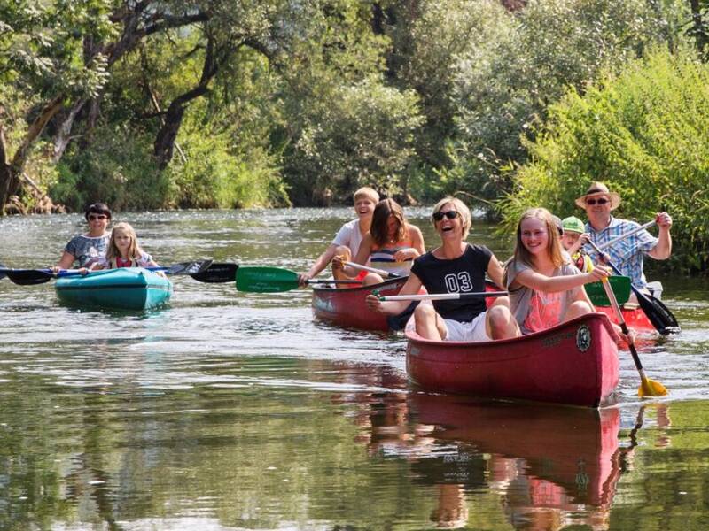 Eine Gruppe von Menschen paddelt in Kanus auf einem von Bäumen gesäumten Fluss.