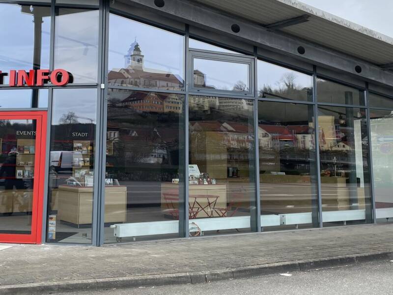Das Bild zeigt ein modernes Gebäude mit Glasfassade und roter Tür, das als Tourist-Info dient.