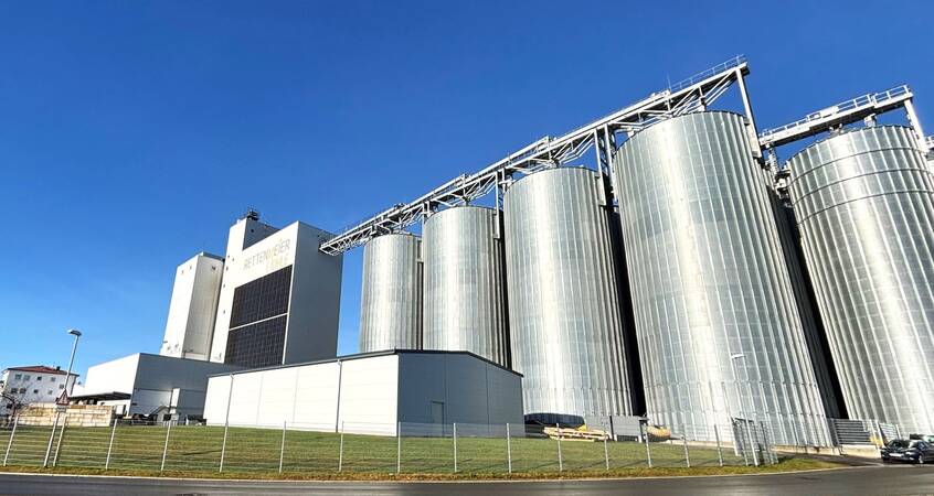 Die Abbildung zeigt eine Reihe von großen, silbernen Silos und einem angrenzenden Gebäude mit klarem, blauem Himmel im Hintergrund.