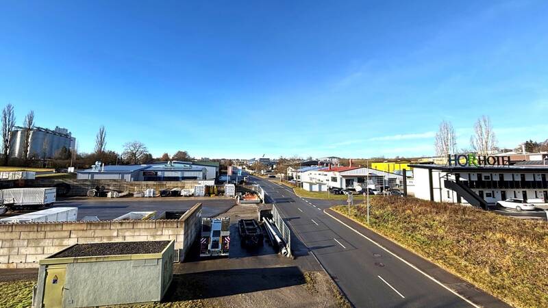 Die Aufnahme zeigt das Industriegebiet Heiligenfeld mit mehreren Gebäuden, geparkten Lastwagen und einem Hotel entlang einer Straße bei klarem Himmel.