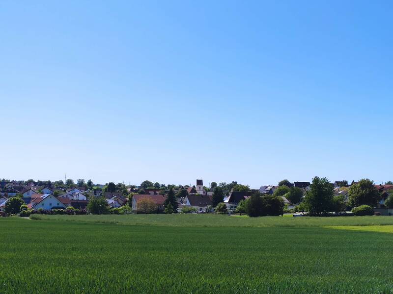 Grünes Feld vor einer Reihe von Häusern unter klarem blauem Himmel.