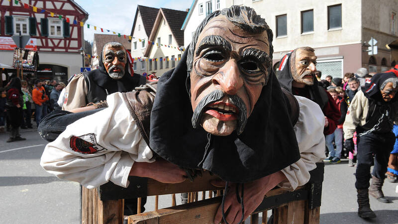 Personen tragen traditionelle Holzmasks während eines Festumzugs in einer deutschen Stadt.