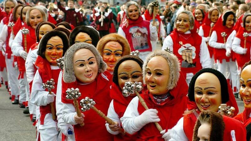 Personen tragen traditionelle Holzmasks während eines Festumzugs in einer deutschen Stadt.