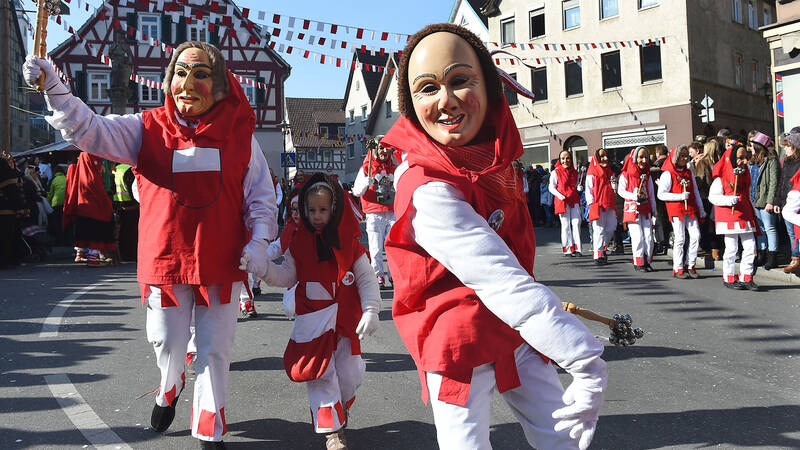 Personen tragen traditionelle Holzmasks während eines Festumzugs in einer deutschen Stadt.