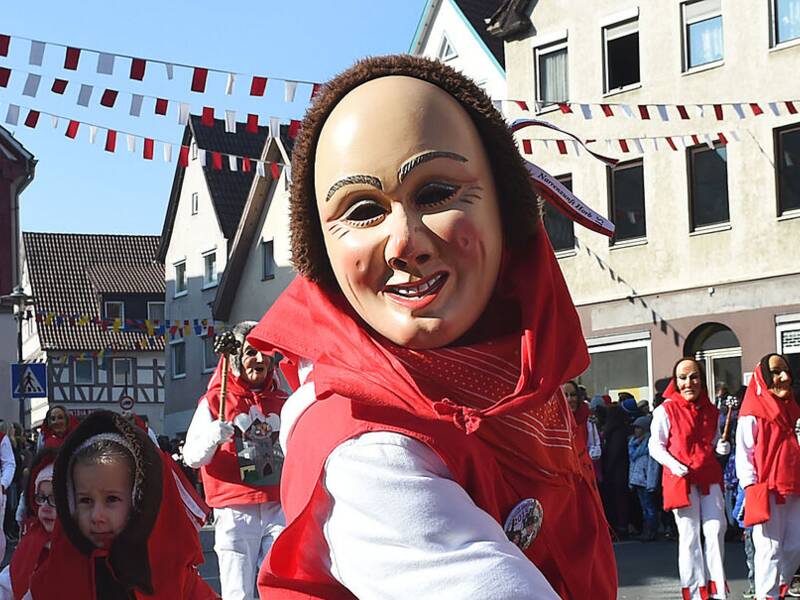 Personen tragen traditionelle Holzmasks während eines Festumzugs in einer deutschen Stadt.