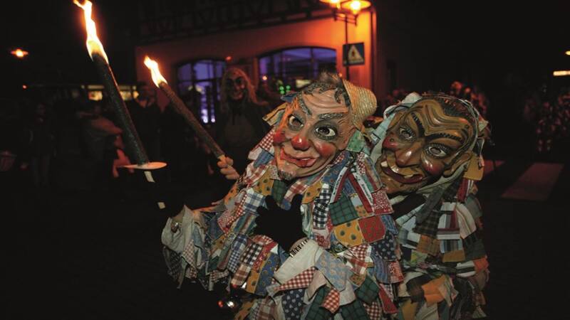 Personen tragen traditionelle Holzmasks während eines Festumzugs in einer deutschen Stadt.