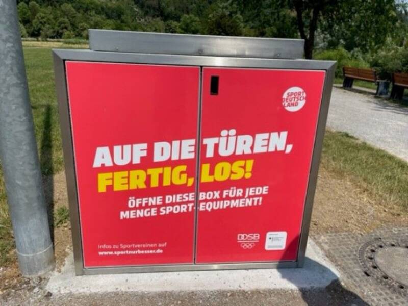 Das Bild zeigt einen roten Schrank und im Hintergrund grüne Bäume und Wiese.