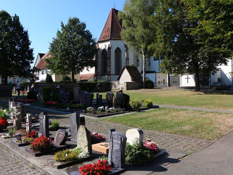 Ein Friedhof mit mehreren Grabsteinen und Blumenarrangements unter einem blauen Himmel.