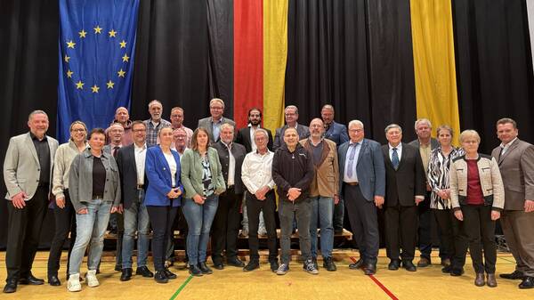 Eine Gruppe von etwa 25 Personen steht in einem Raum vor großen EU- und deutschen Flaggen und posiert für ein Gruppenfoto.
