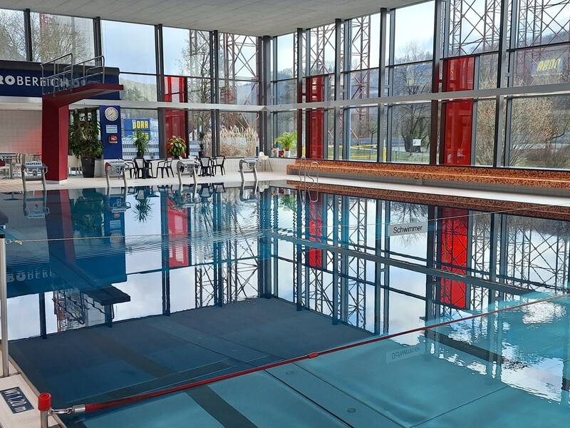 Ein geräumiges Hallenbad mit großen Fenstern und einem angrenzenden Gastronomiebereich.