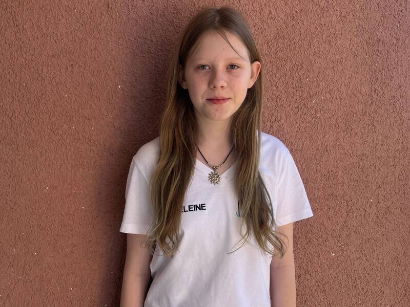 Ein Mädchen mit langen Haaren und einem weißen T-Shirt steht vor einer strukturieren roten Wand.