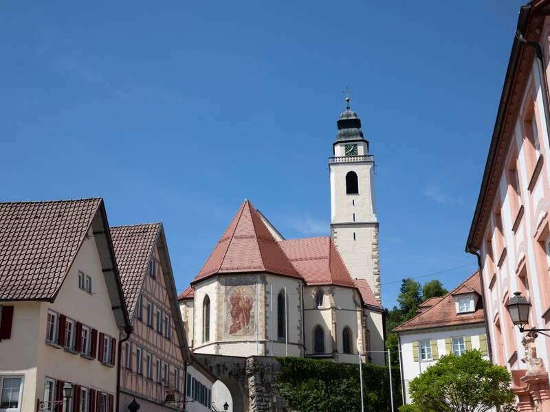 Auf dem Bild ist eine Kirche zu sehen, die leicht erhöht, neben mehreren historischen Gebäuden steht.