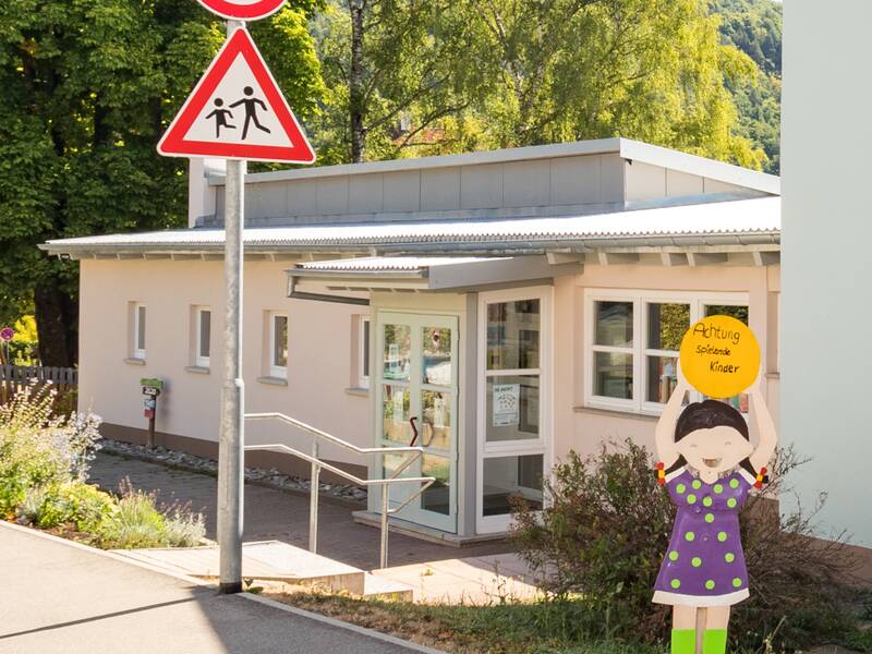Eingangsbereich mit Hinweisschild auf spielende Kinder und Geschwindigkeitsbegrenzung 30km/h. Rechts eine Mädchenfigur mit Hinweis auf spielende Kinder.