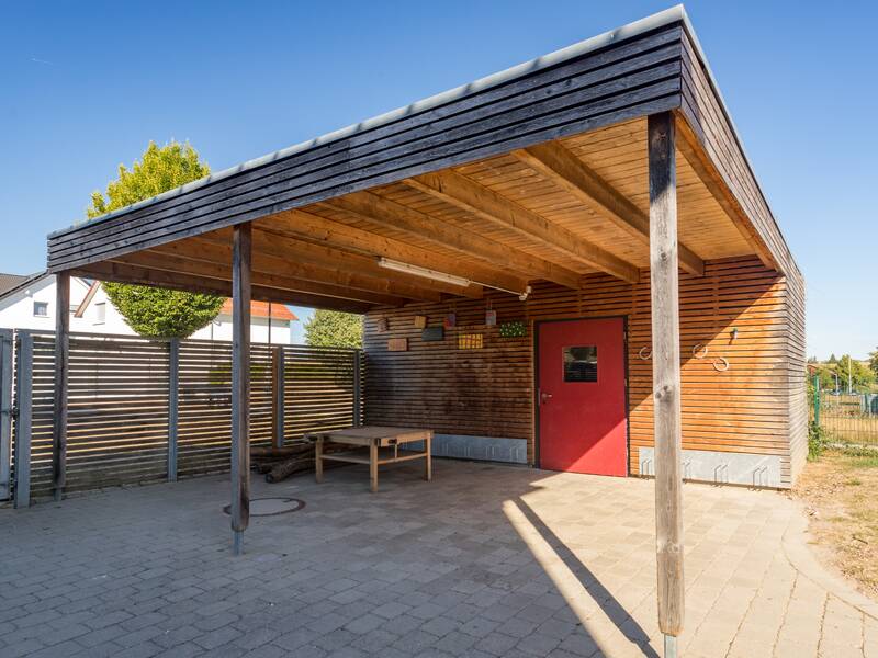 Überdachter Außenplatz mit Spielgeräteschuppen.