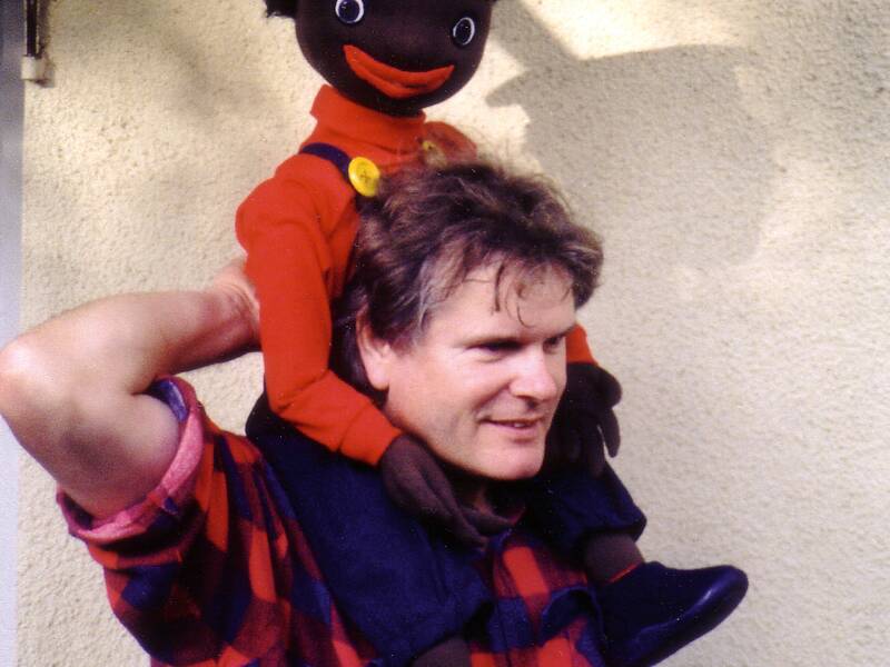 Ein Mann trägt eine große Puppe, die ein fröhliches Gesicht und eine Uniformmütze trägt, auf seinen Schultern.