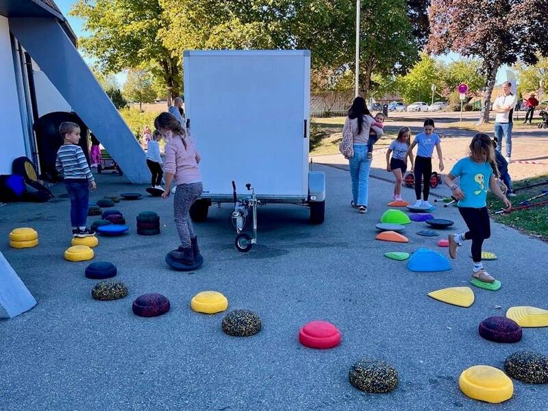 Kinder spielen vor einem Gebäude auf einem Outdoor-Parcours mit bunten Balanciersteinen auf dem Boden.
