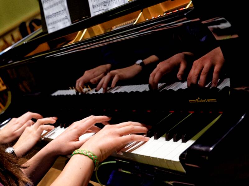 Hände zweier Personen spielen am Klavier.