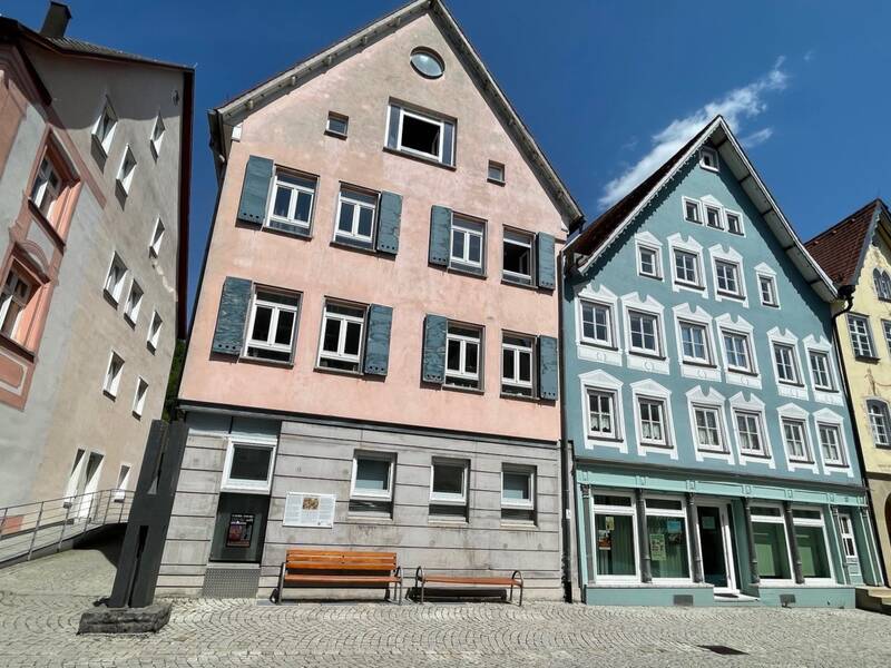 Mehrere historische Gebäude mit Fachwerk und Satteldach mit blauem Himmel und Sitzbänken davor.