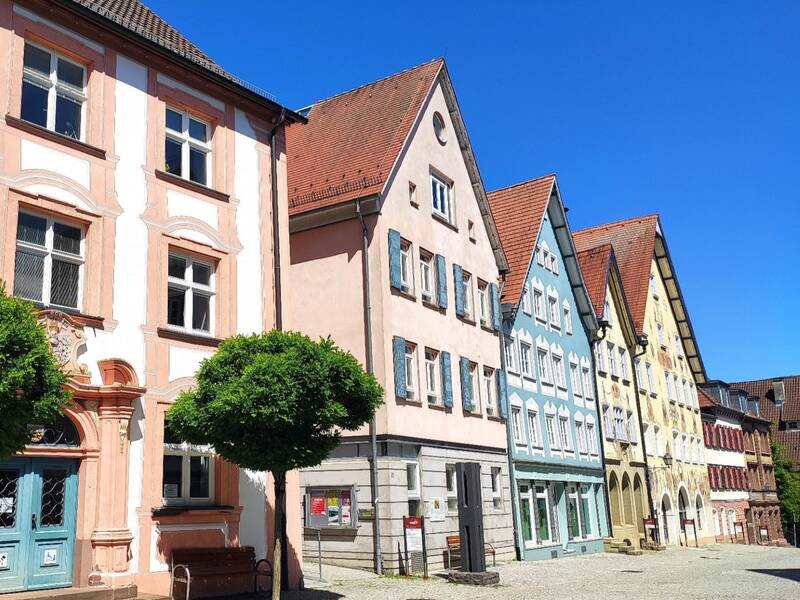 Reihe historischer Fachwerkhäuser mit bunten Fassaden und spitzen Dächern unter klarem blauem Himmel.
