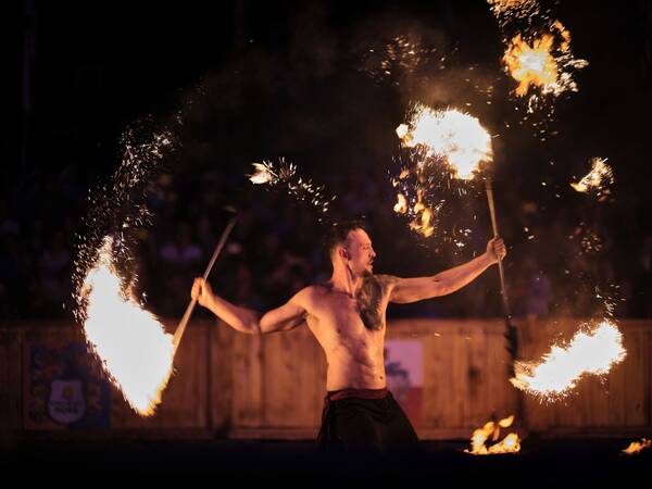 Ein Mann mit nacktem Oberkörper führt in der Dunkelheit eine Feuershow mit brennenden Stäben auf.