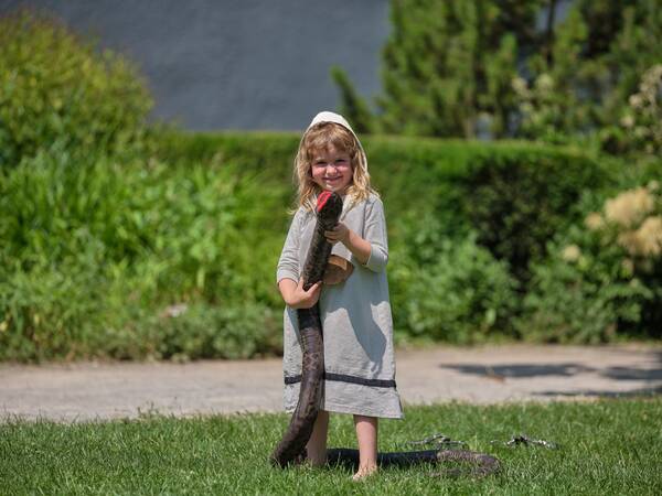 Ein lächelndes kleines Mädchen steht auf einer Wiese und hält eine große Schlange in den Händen.
