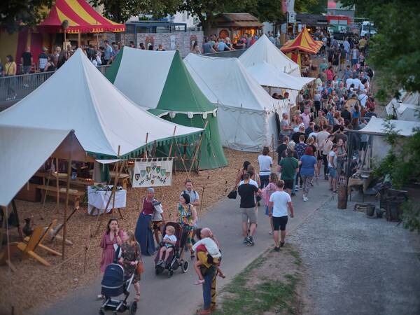 Auf einem lebhaften Mittelaltermarkt spazieren Menschen zwischen weißen und bunten Zelten entlang.
