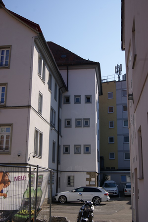 Innenhof mit weißen und gelben Wohngebäuden, mehreren geparkten Autos und einem Motorrad im Vordergrund.