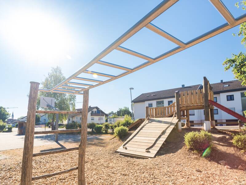 Das Bild zeigt einen Spielplatz mit einem Klettergerüst und einer Rutsche. 