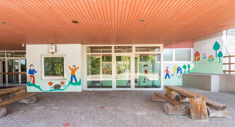Das Bild zeigt den Schuleingang mit bunter Fensterdekoration.